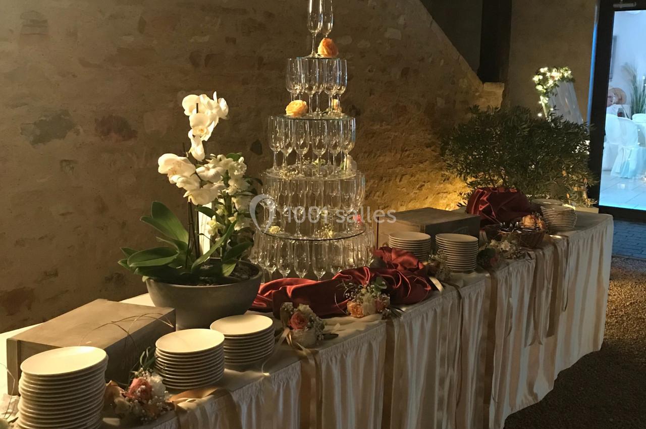 Table de réception décorée avec des assiettes, des fleurs, et une pyramide de verres surmontée de fruits.