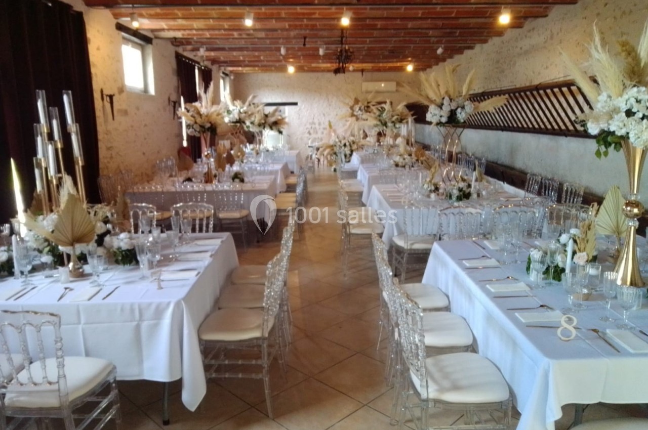 Salle de réception décorée avec des tables dressées, chaises transparentes et arrangements floraux élégants.