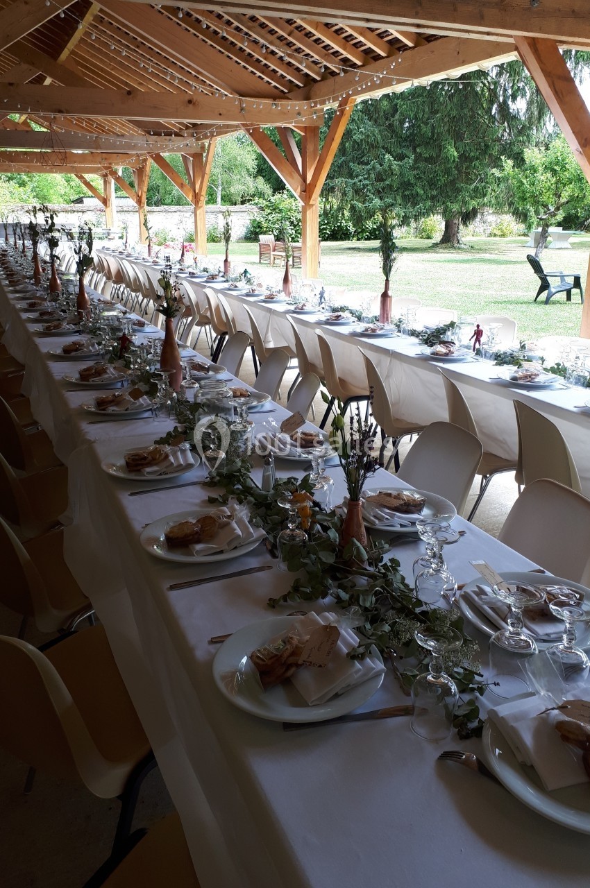 Tables longues décorées pour un repas festif sous une structure en bois, avec vue sur un jardin verdoyant.