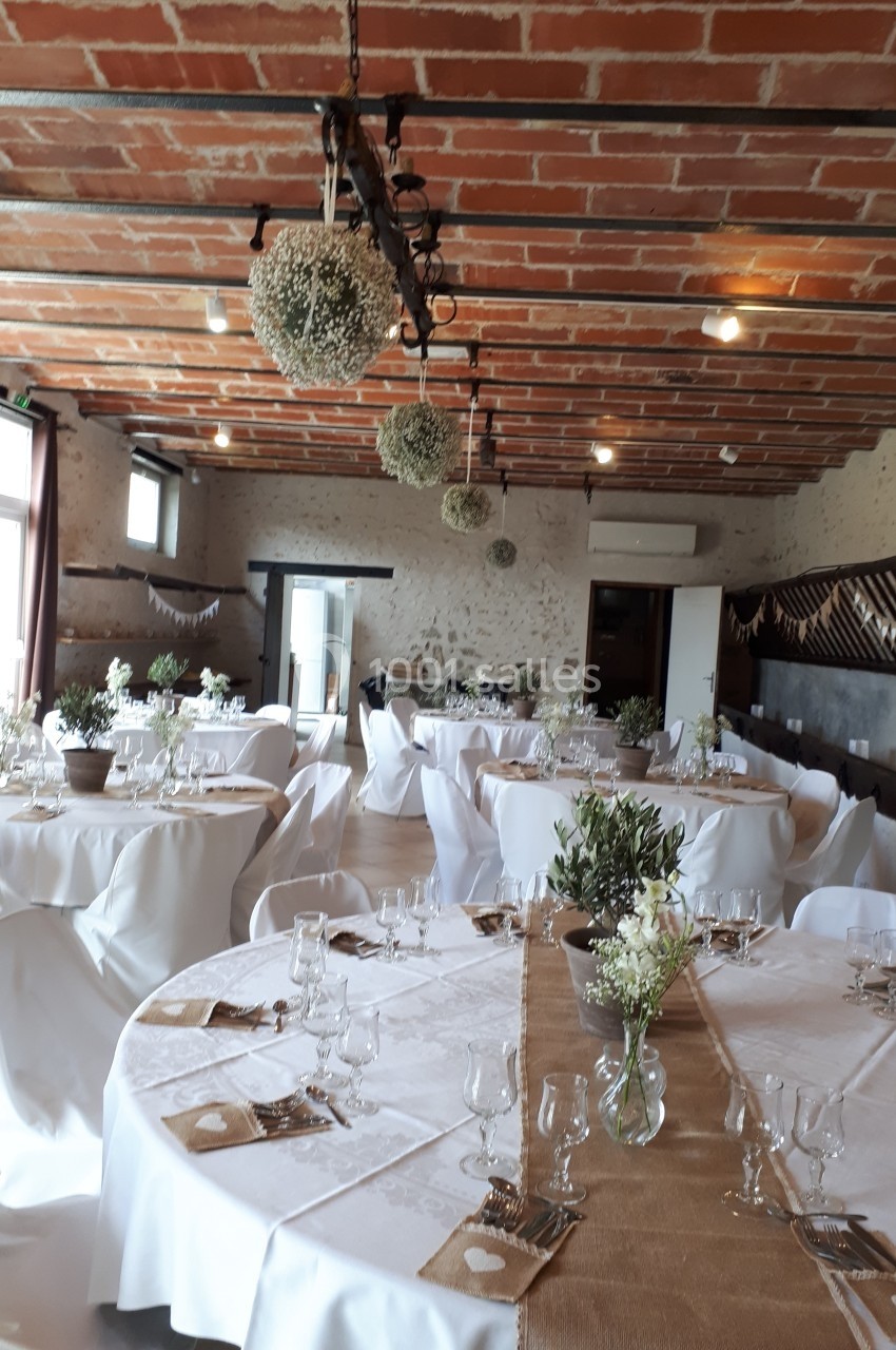 Salle de réception décorée avec des tables rondes dressées, nappes blanches et éléments floraux suspendus.