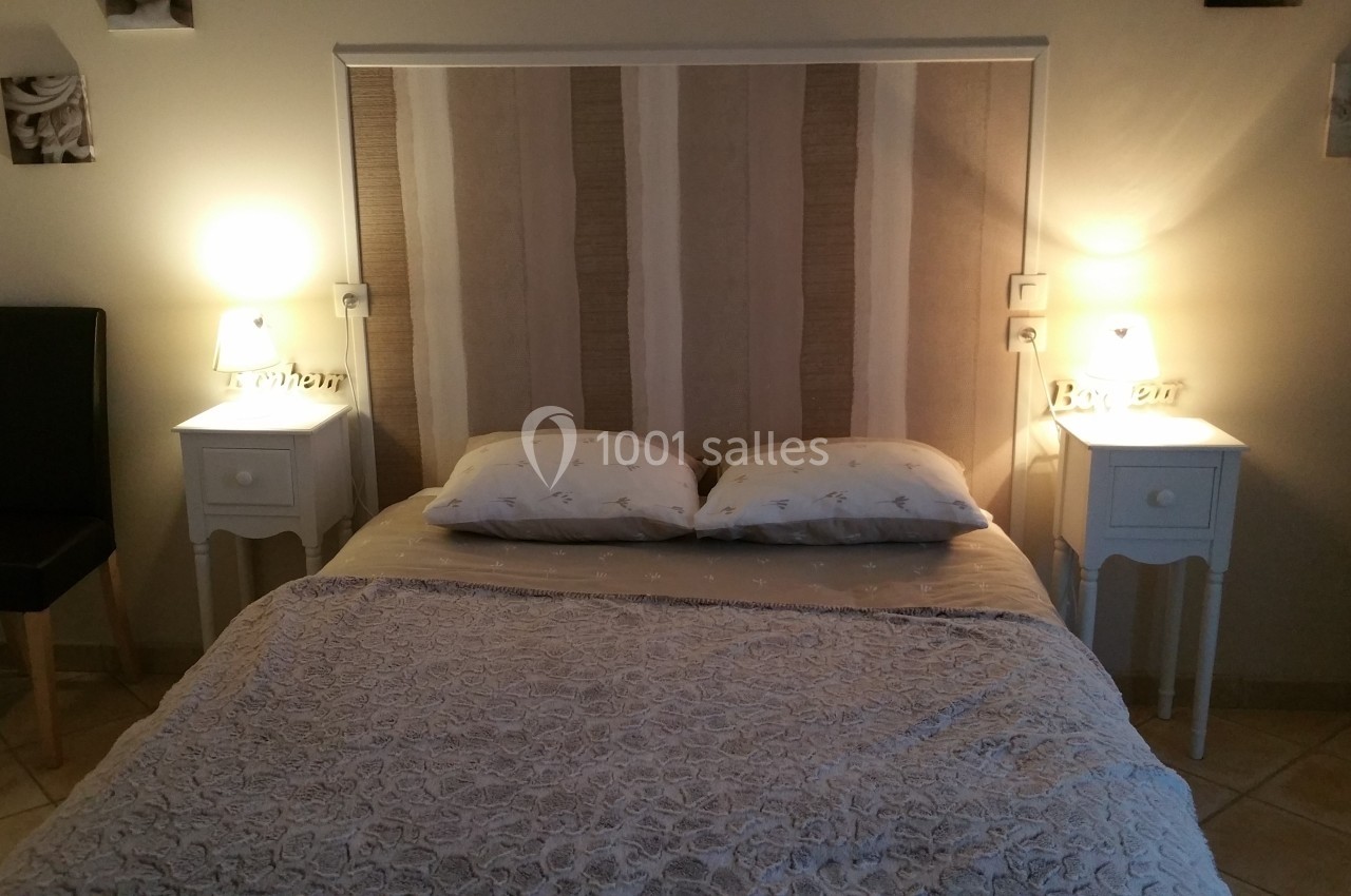 Lit double avec tête de lit rayée, deux tables de chevet blanches et lampes allumées dans une chambre sobre.