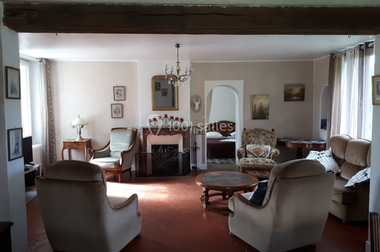 Salon lumineux avec mobilier ancien, cheminée décorative, fauteuils et table basse sur un sol en terre cuite.