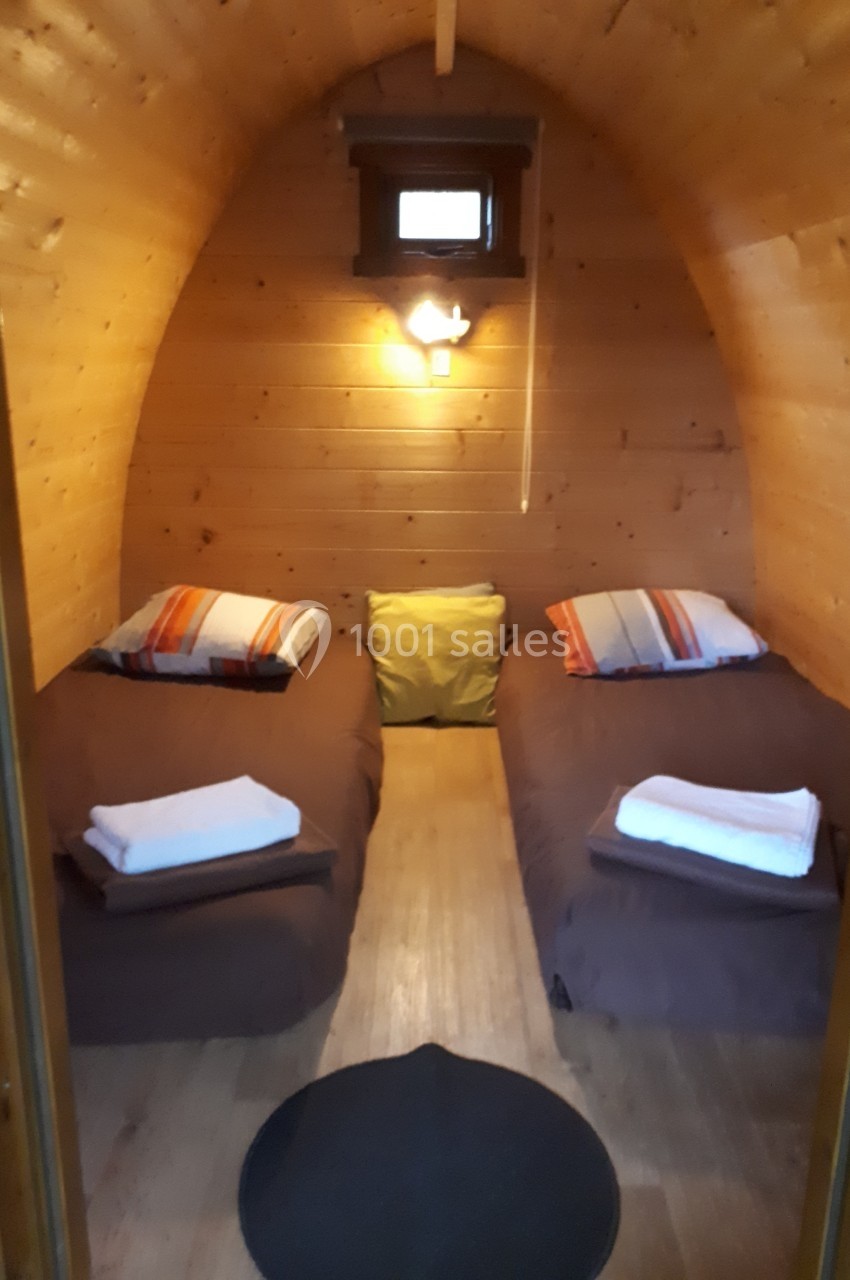 Intérieur d'une cabane en bois avec deux lits simples, linge de lit plié et lumière douce au mur.