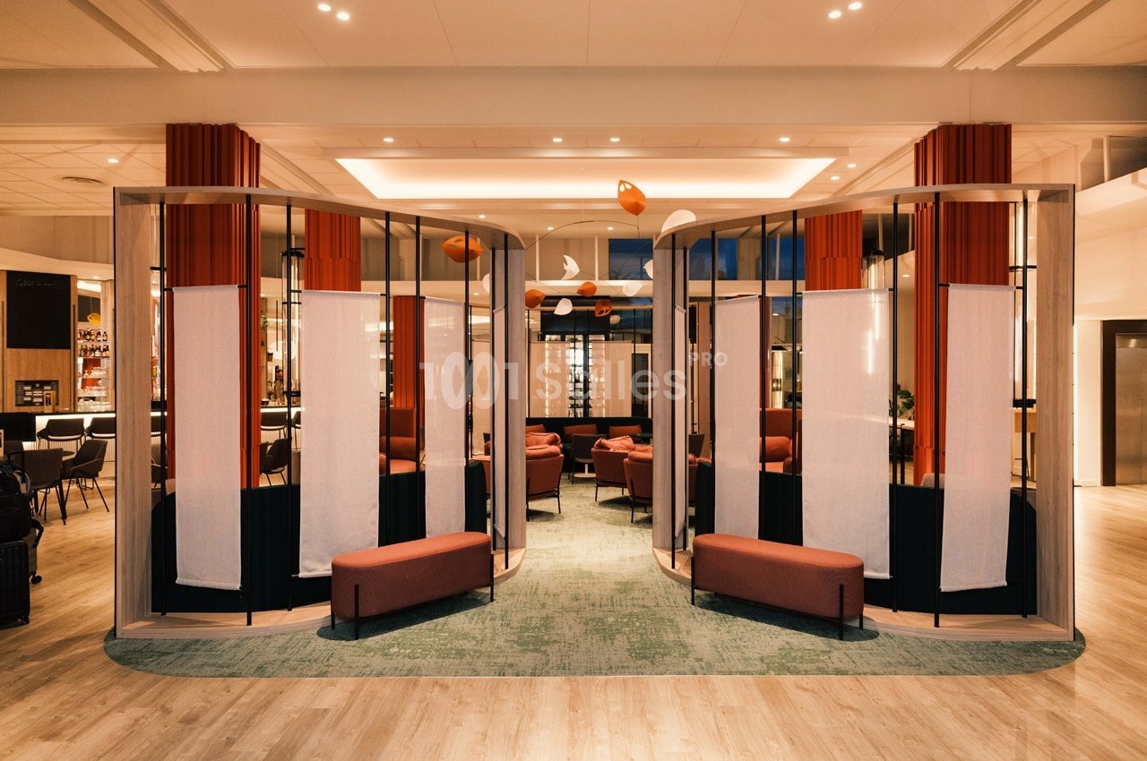 Espace intérieur moderne avec cloison semi-ouverte, fauteuils rouges et éclairage chaleureux.