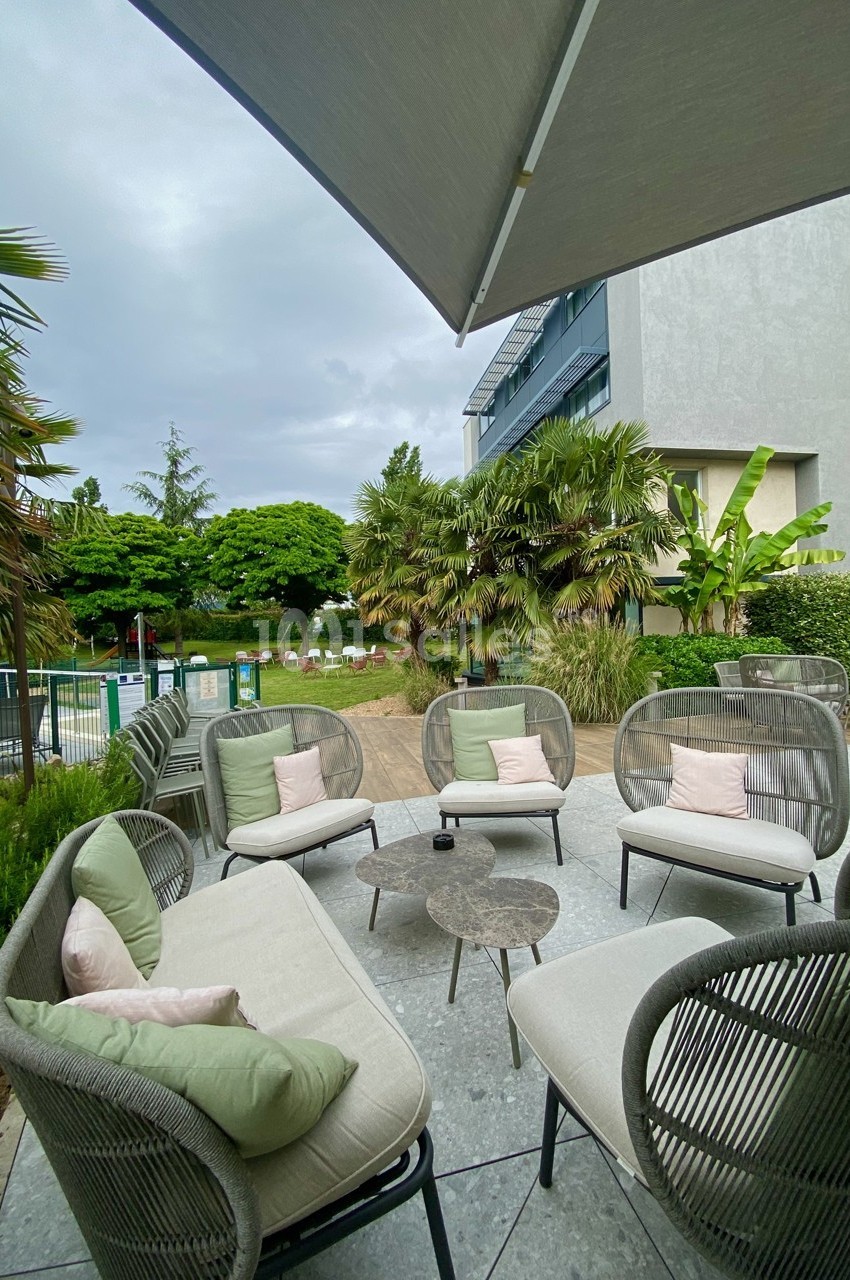 Salon de jardin avec fauteuils et table basse sur une terrasse, entouré de végétation tropicale et proche d'une piscine.