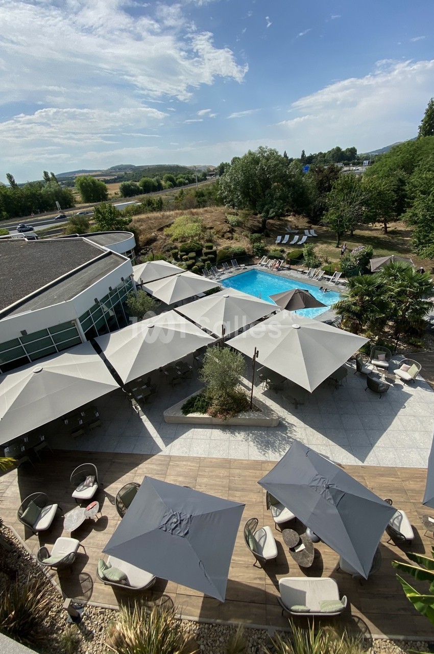 Vue aérienne d'une terrasse avec parasols, piscine extérieure et espaces verts environnants par temps ensoleillé.
