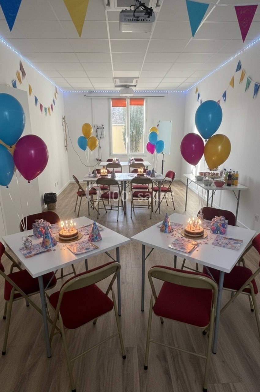Salle décorée pour une fête, avec ballons colorés, guirlandes, tables dressées et gâteaux d'anniversaire allumés.