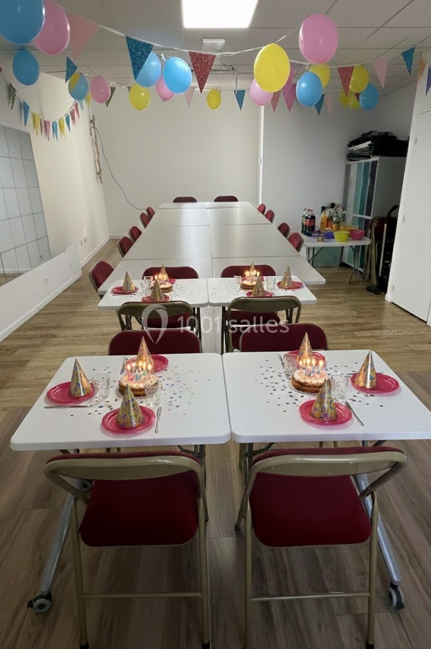 Salle décorée pour une fête avec ballons, guirlandes, tables dressées et chapeaux de fête colorés.