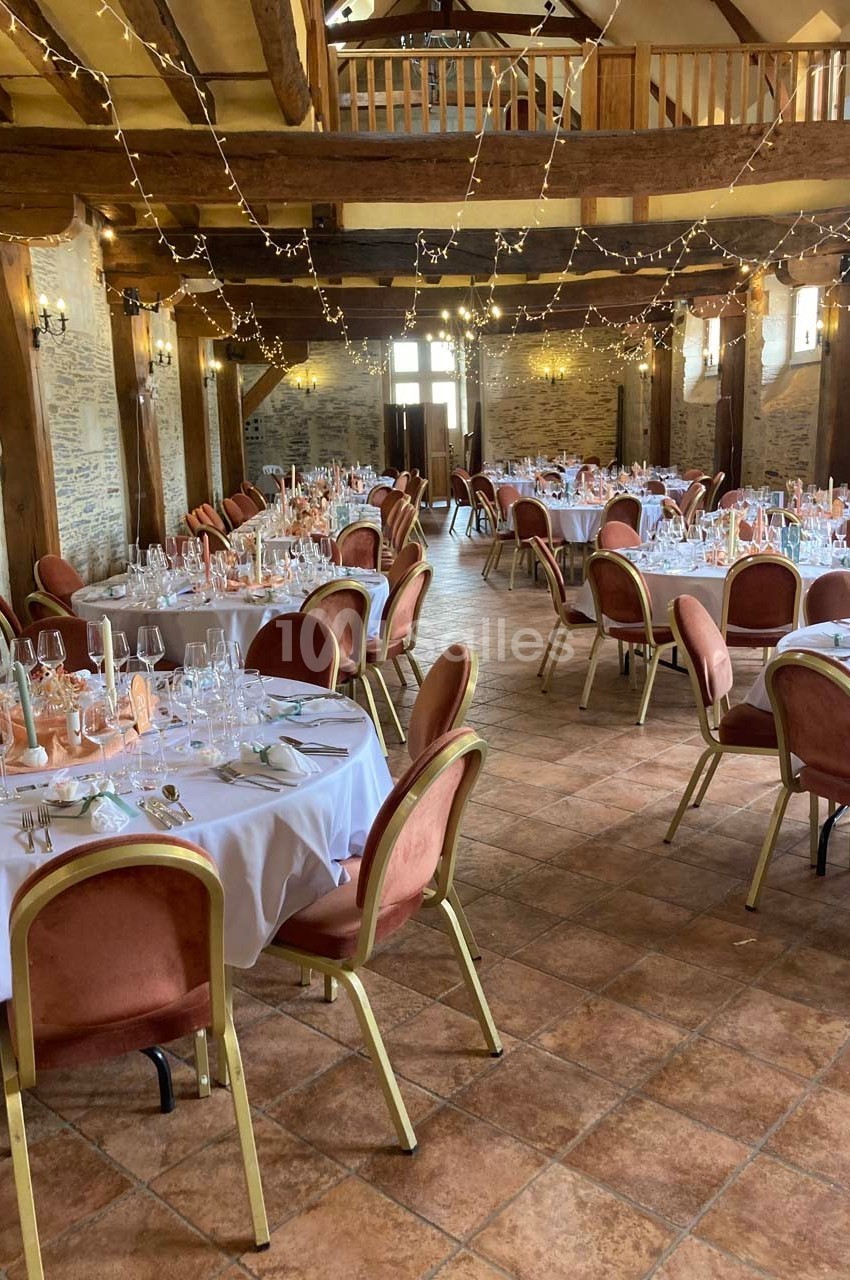 Salle de réception décorée avec des tables rondes dressées, chaises rouges et guirlandes lumineuses suspendues.