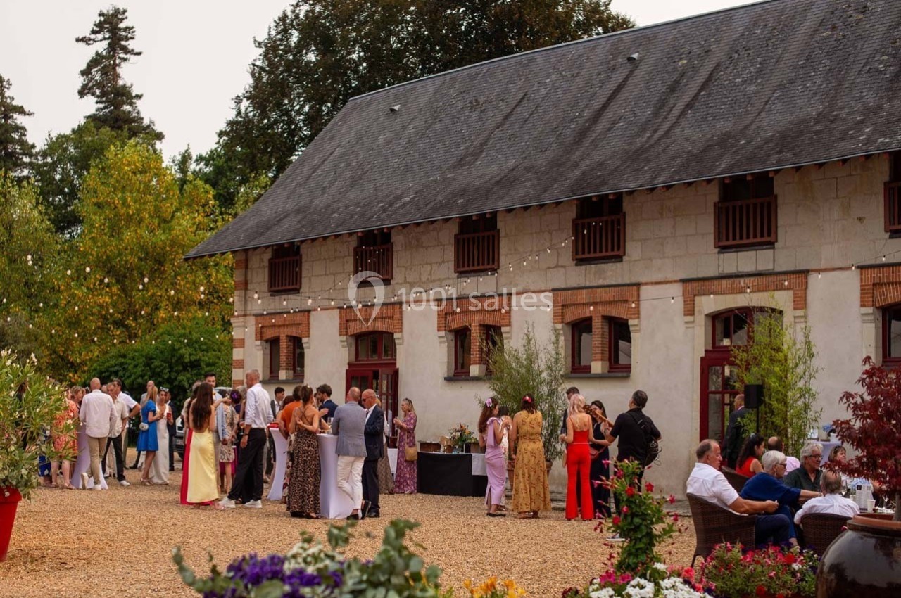 Groupe de personnes rassemblées devant un bâtiment en pierre avec toit en ardoise, entouré de végétation et de décorations…