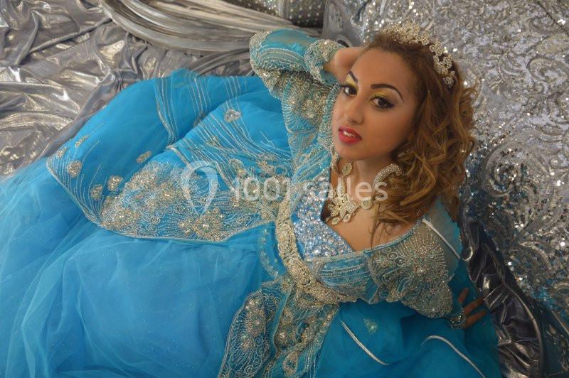 Femme portant une robe traditionnelle bleue ornée de broderies argentées, posant sur un fond scintillant.