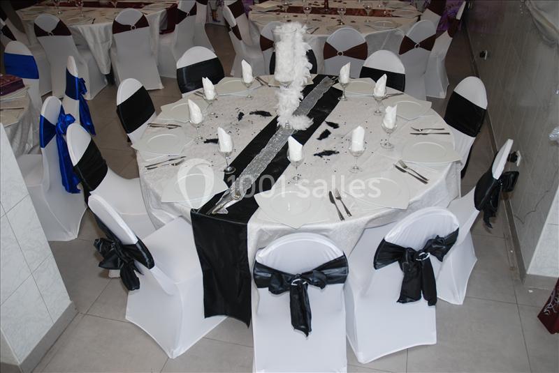 Table ronde décorée pour une réception, avec nappes blanches, chemins de table noirs et chaises ornées de nœuds noirs.