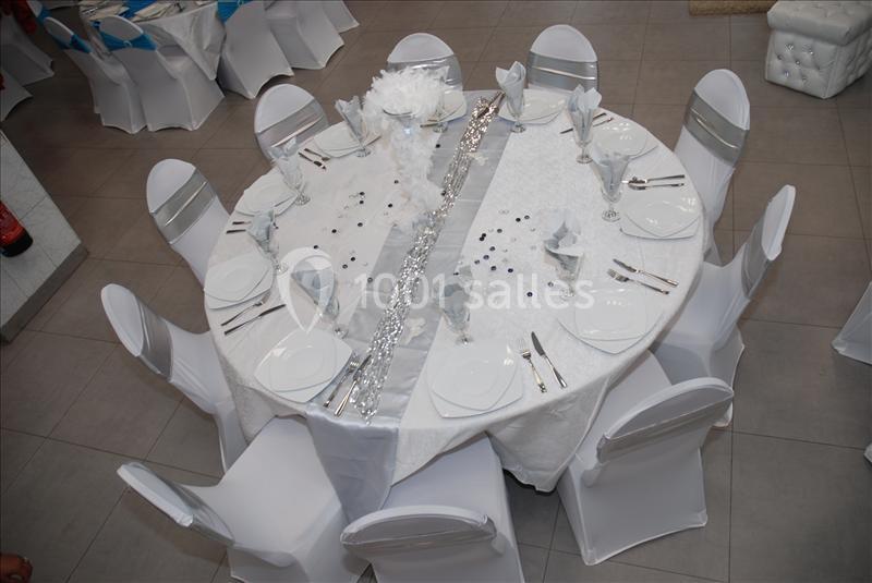 Table ronde dressée pour un événement, nappée de blanc avec des couverts, serviettes pliées et décoration centrale.