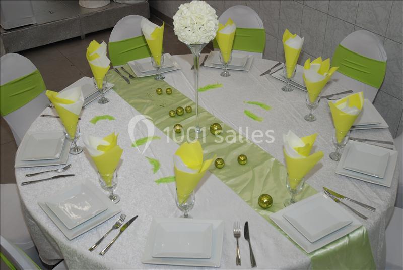 Table ronde décorée avec une nappe blanche, des serviettes jaunes pliées, des éléments verts et un centre de table floral.