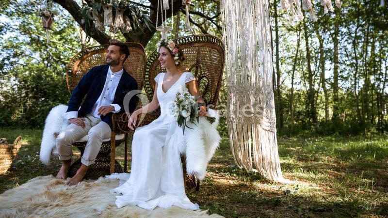 Un couple assis sur des fauteuils en osier, dans un décor bohème en extérieur, entouré de verdure et de macramés.