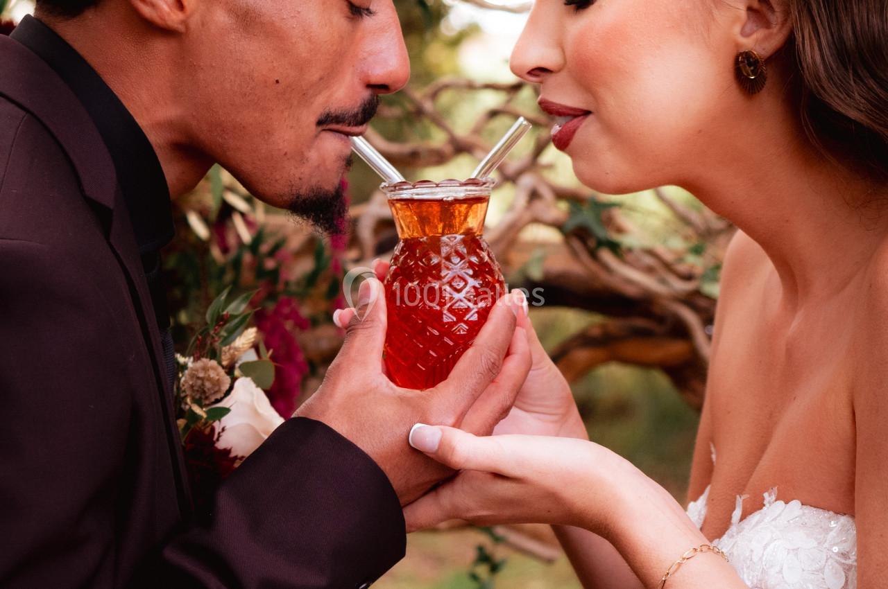 Un couple partage une boisson dans un verre en forme d'ananas lors d'une célébration en plein air.