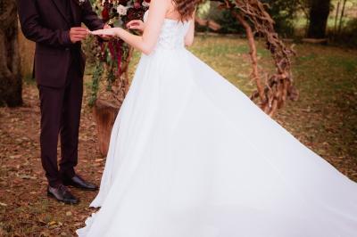 Un couple en tenue de mariage se regarde sous une pergola illuminée de guirlandes lumineuses.