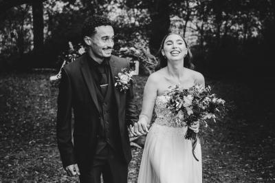 Un couple en tenue de mariage se regarde sous une pergola illuminée de guirlandes lumineuses.