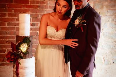 Un couple en tenue de mariage se regarde sous une pergola illuminée de guirlandes lumineuses.