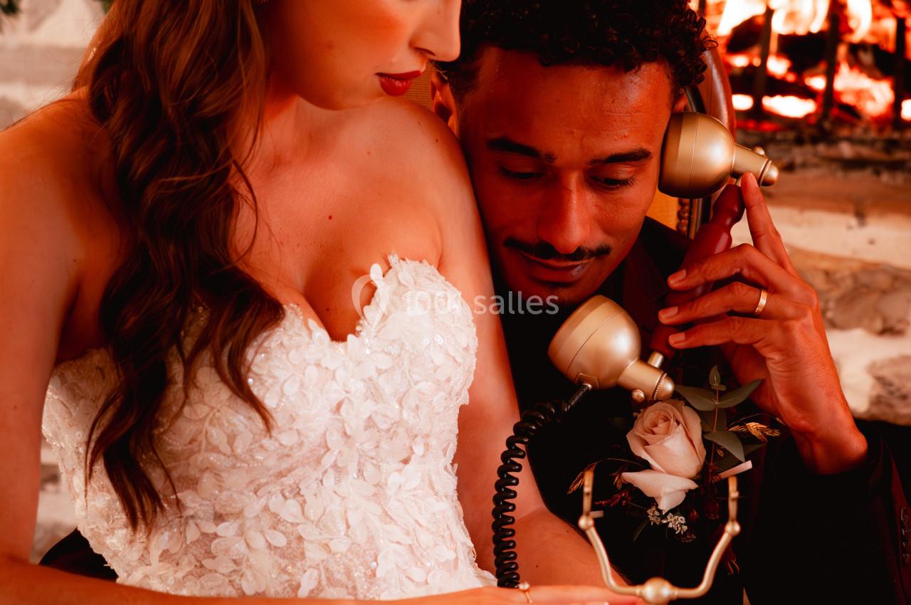 Un couple en tenue élégante partage un moment intime près d'une cheminée, utilisant un téléphone vintage.
