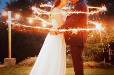 Un couple en tenue de mariage se regarde sous une pergola illuminée de guirlandes lumineuses.