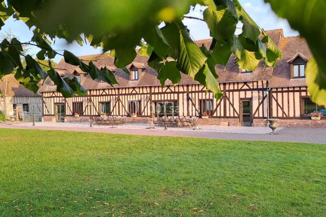 Bâtiment à colombages entouré de pelouse, partiellement encadré par des feuilles au premier plan.