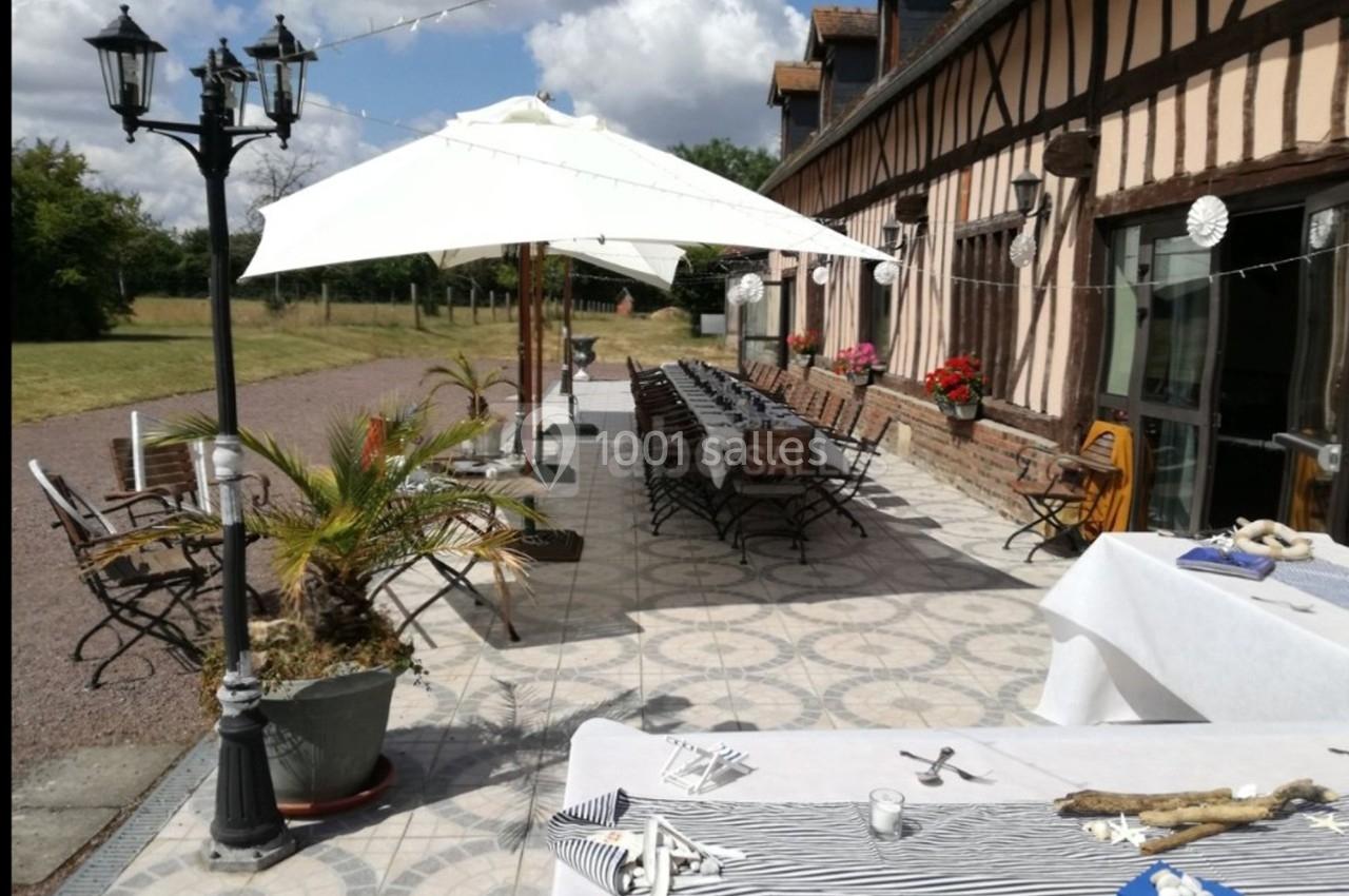 Terrasse extérieure avec tables dressées, parasols blancs, lampadaire et bâtiment à colombages en arrière-plan.