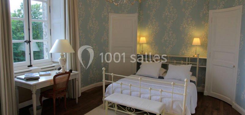 Chambre lumineuse avec lit en métal blanc, bureau près d'une fenêtre et murs décorés de papier peint bleu à motifs.