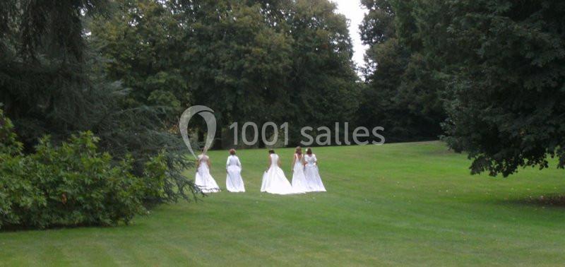 Des femmes en robes blanches marchent sur une pelouse verte entourée d'arbres dans un parc.