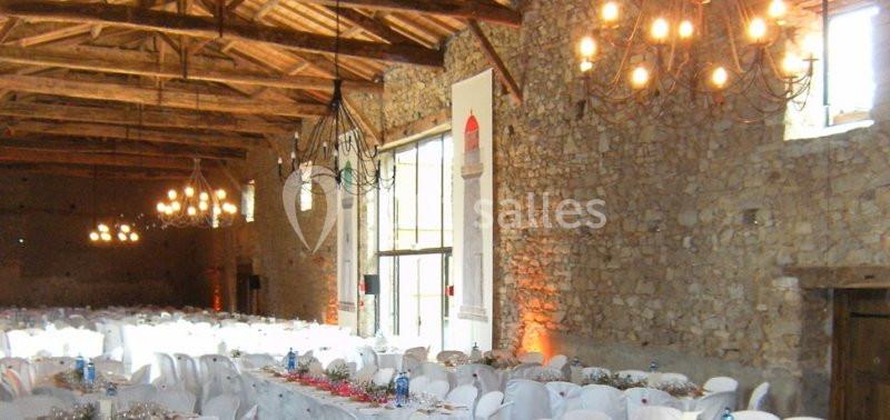 Salle de réception en pierre avec plafond en bois, tables dressées et lustres suspendus.