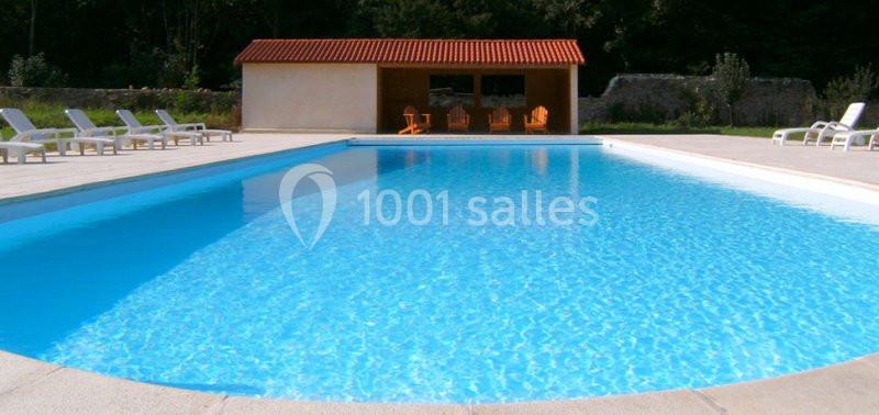 Piscine extérieure rectangulaire avec eau claire, entourée de chaises longues et d'un bâtiment à toit rouge.