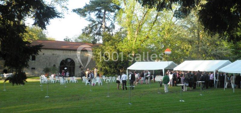 Des invités rassemblés sous des tentes blanches dans un jardin verdoyant, près d'un bâtiment en pierre.
