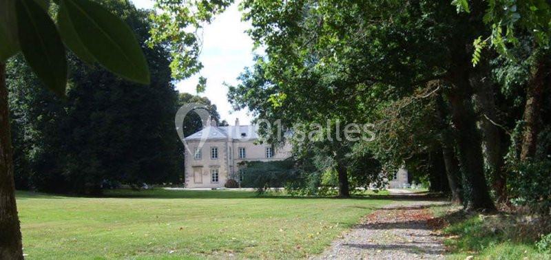 Allée bordée d'arbres menant à un grand bâtiment en pierre entouré de pelouse et de végétation.